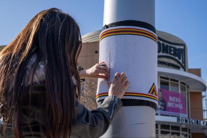 a woman fixes bead art to a street pole