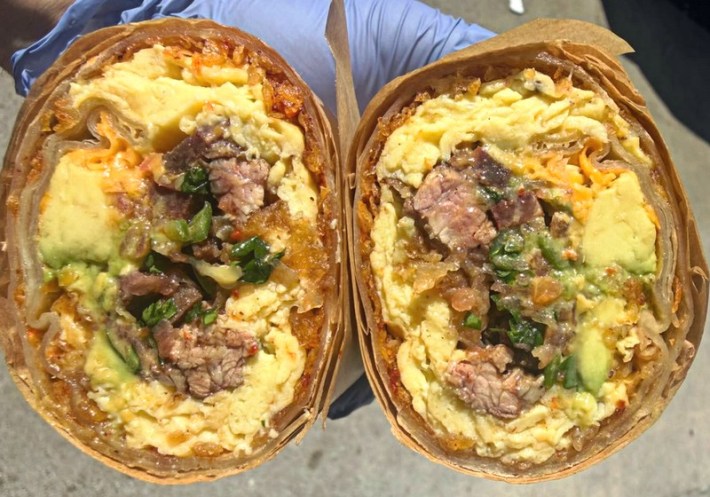 A burrito sliced in half, showing insides with beef kebab, cheese, eggs, and salsa.