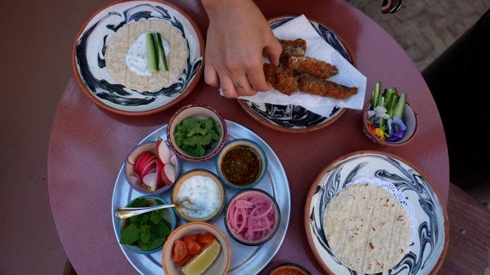 plates of tortillas, fried sardines, and toppings (cucumber, radish, pickled onion, herbs, and sauces)