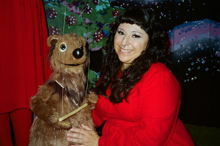 a bear puppet (left) and a woman with dark hair smiling (right)