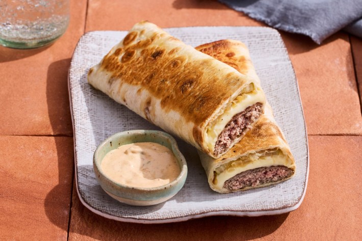 A cheeseburger wrap next to a small bowl of sauce from Mini Kabob at Neighborly.