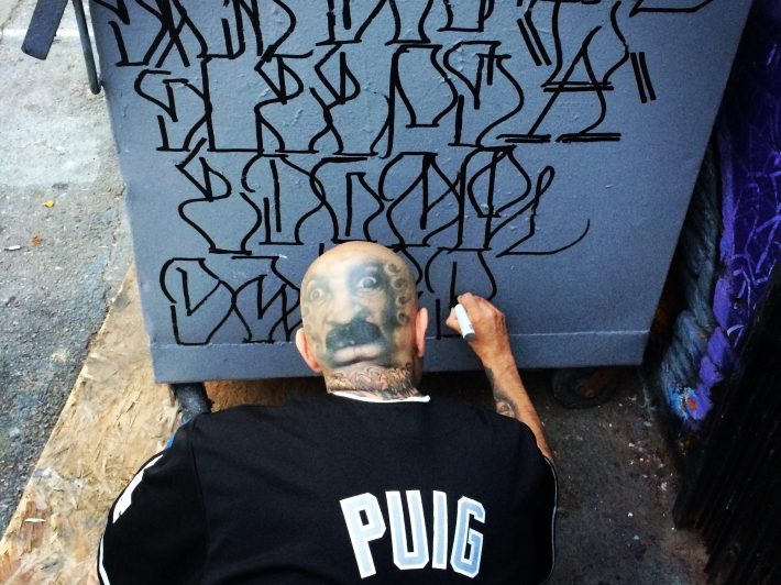 a man uses a marker to draw on a dumpster outside