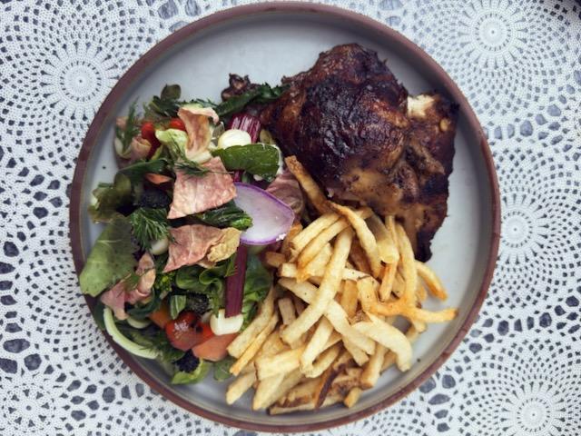 A plate with Peruvian chicken, fries, and salad on a crocheted tablecoth