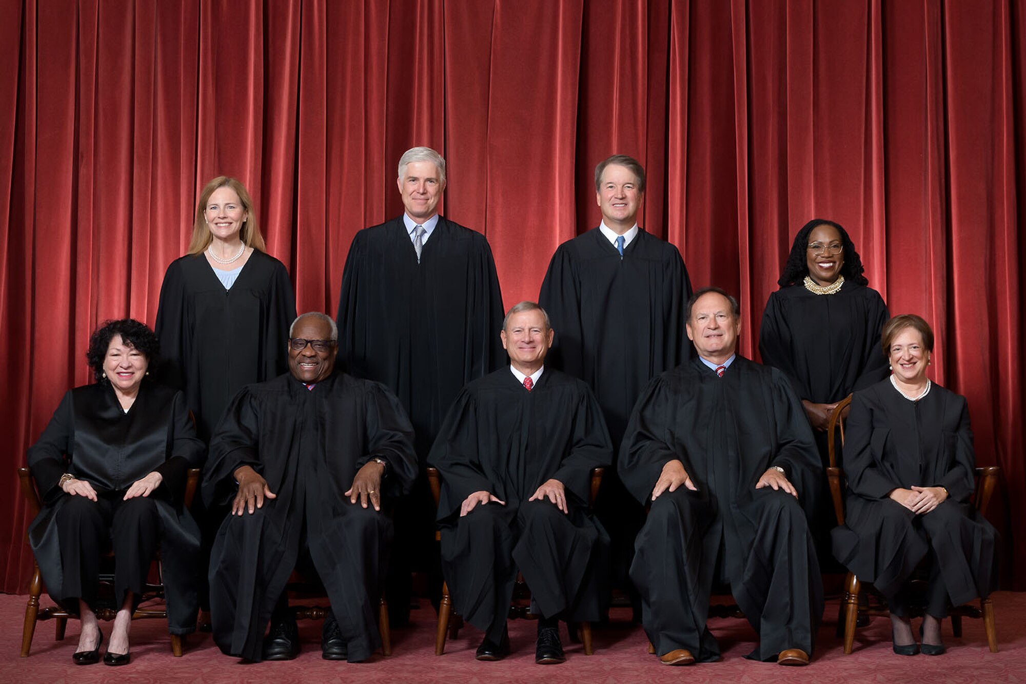 Formal group photograph of the Supreme Court as it was been comprised on June 30, 2022 after Justice Ketanji Brown Jackson joined the Court. The Justices are posed in front of red velvet drapes and arranged by seniority, with five seated and four standing. Seated from left are Justices Sonia Sotomayor, Clarence Thomas, Chief Justice John G. Roberts, Jr., and Justices Samuel A. Alito and Elena Kagan. Standing from left are Justices Amy Coney Barrett, Neil M. Gorsuch, Brett M. Kavanaugh, and Ketanji Brown Jackson. Credit: Fred Schilling, Collection of the Supreme Court of the United States.
