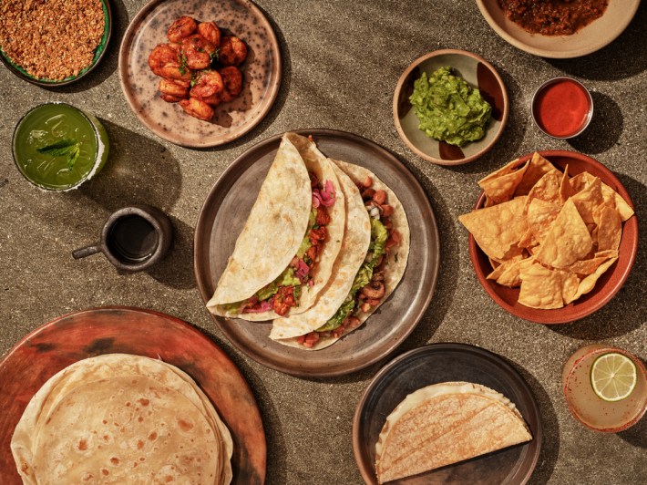 A spread of flour tortillas, chips, guacamole, tacos, quesadillas, and one open taco with shrimp