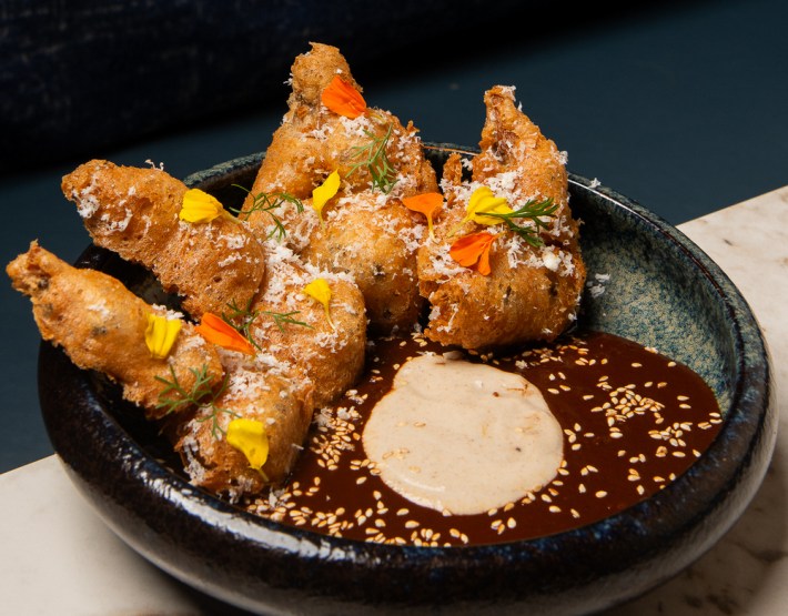 Four umami mushroom tempura pieces in a bowl of mole colorado and plantain puree, sprinkled with cotija cheese and edible flowers.