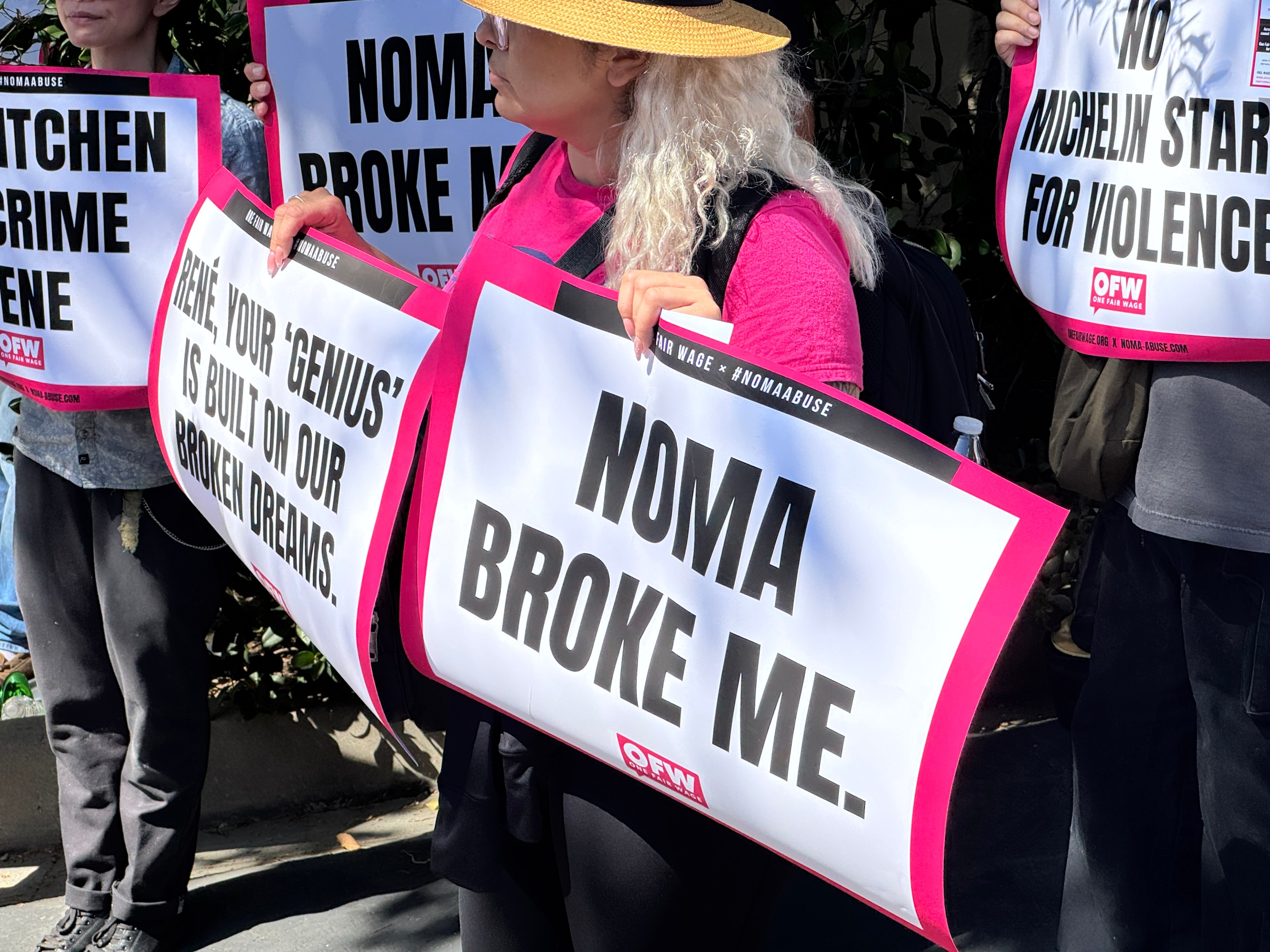An organizer with One Fair Wage holds a sign that says "NOMA BROKE ME" in front of the Paramour Estate in Silver Lake