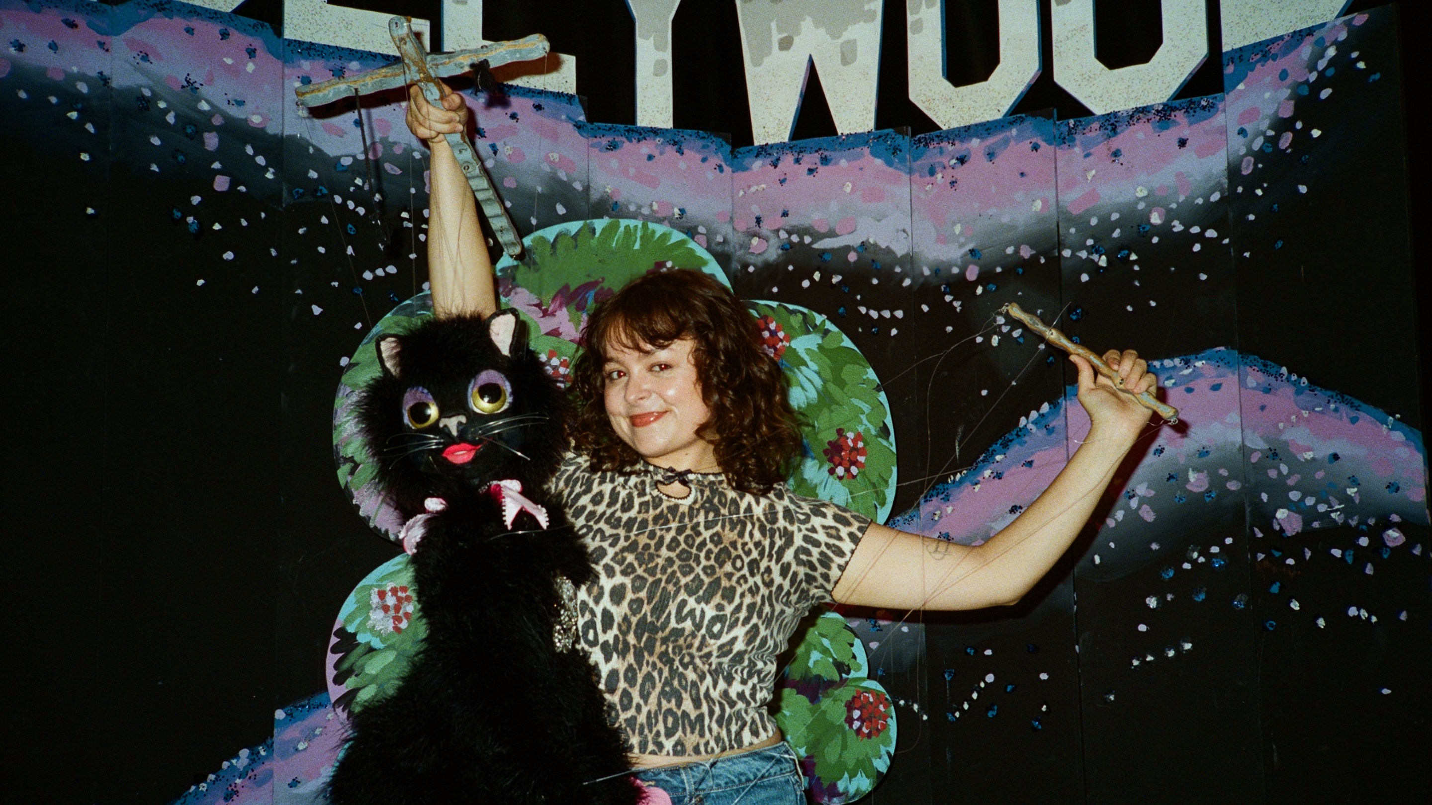 a woman in a cheetah print shirt with a puppet in front of a fake Hollywood sign