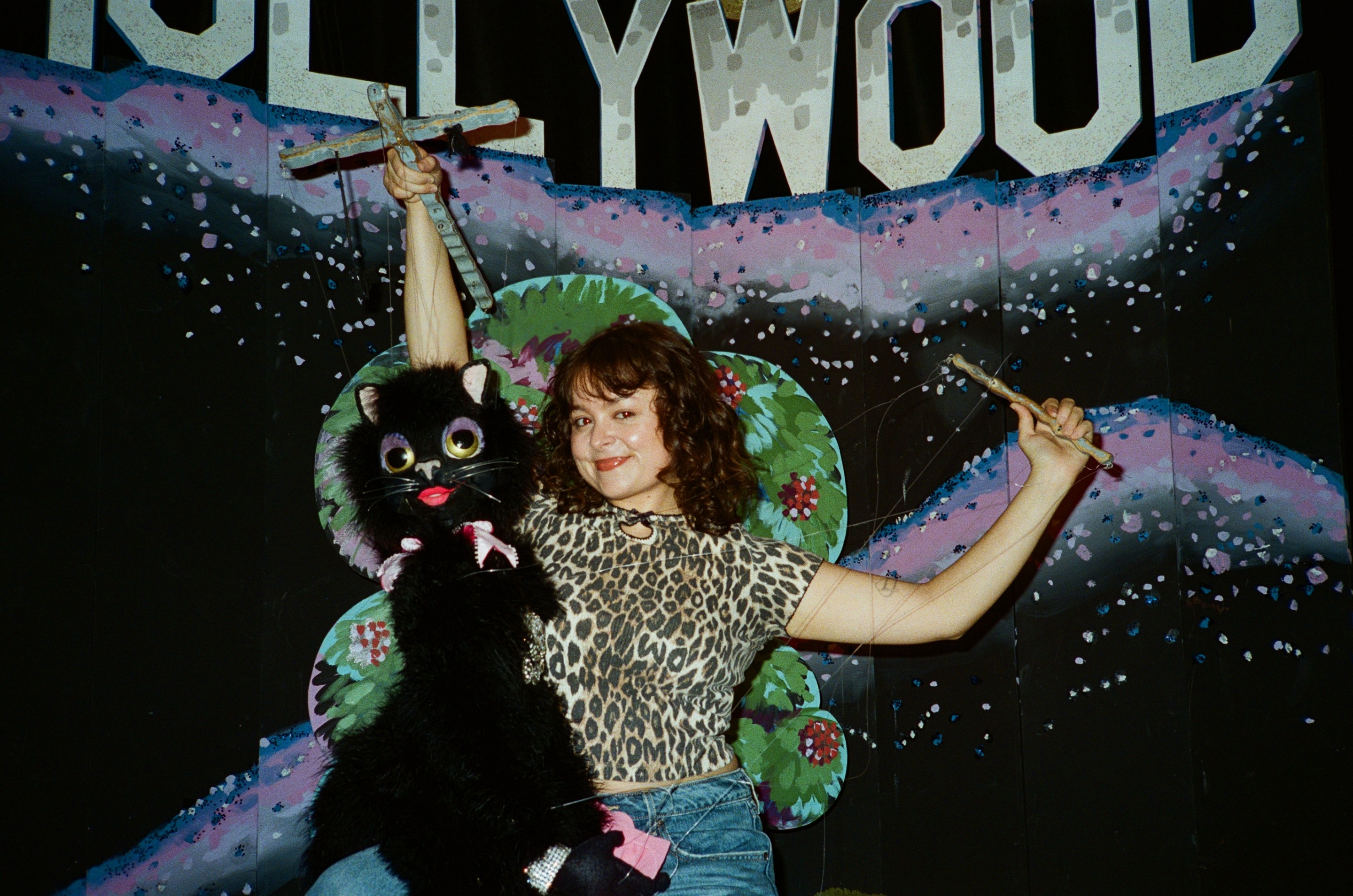 a woman in a cheetah print shirt with a puppet in front of a fake Hollywood sign