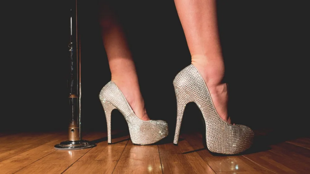 A pair of sparkly high heeled shoes next to the bottom of a pole