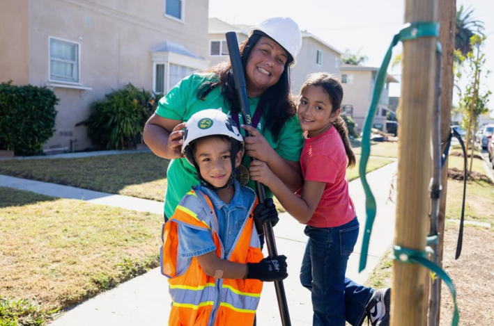 a mother in a hard hat poses with her son wearing a hard hat and high visibility vest, and with her daughter
