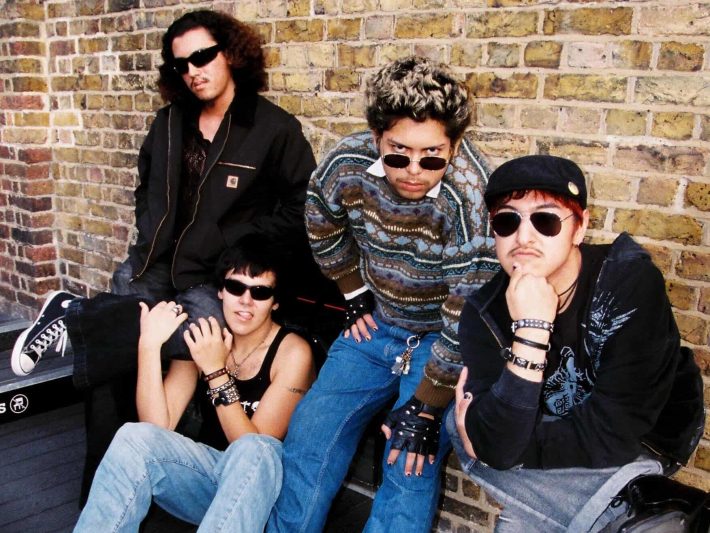 four bandmates posing in front of a brick wall