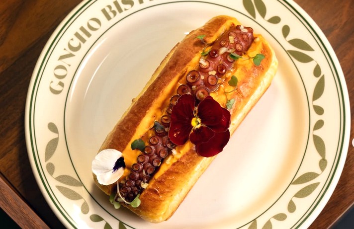 A brioche bun with an octopus tentacle in it and edible flowers on top