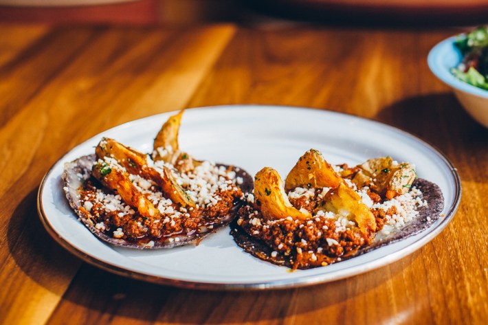 Two tacos with potato and chorizo on blue corn tortillas on a white plate