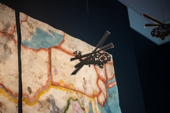 "Book 13" exhibit by Sandy Rodriguez at The Huntington, featuring a close up of a hanging helicopter installed in front of the map