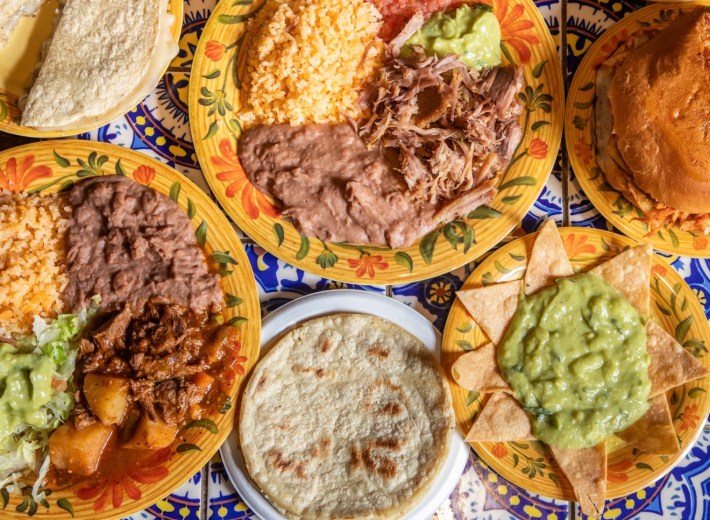 Plates of Mexican food: chips and guacamole, tortillas, plates of meat, beans, and rice