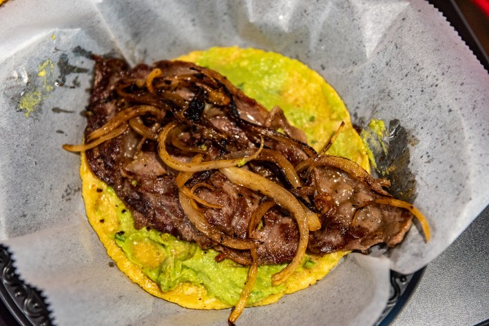 a taco with beef, onions, and guacamole on a corn tortilla