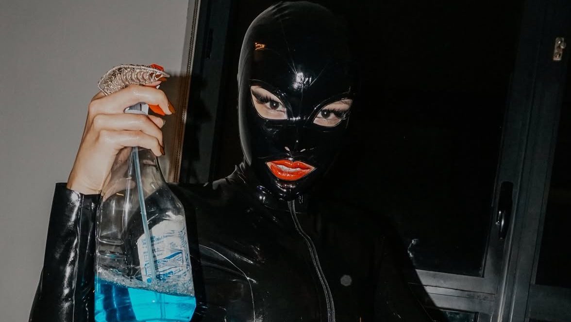 a domme wears a mask and holds a spray gun