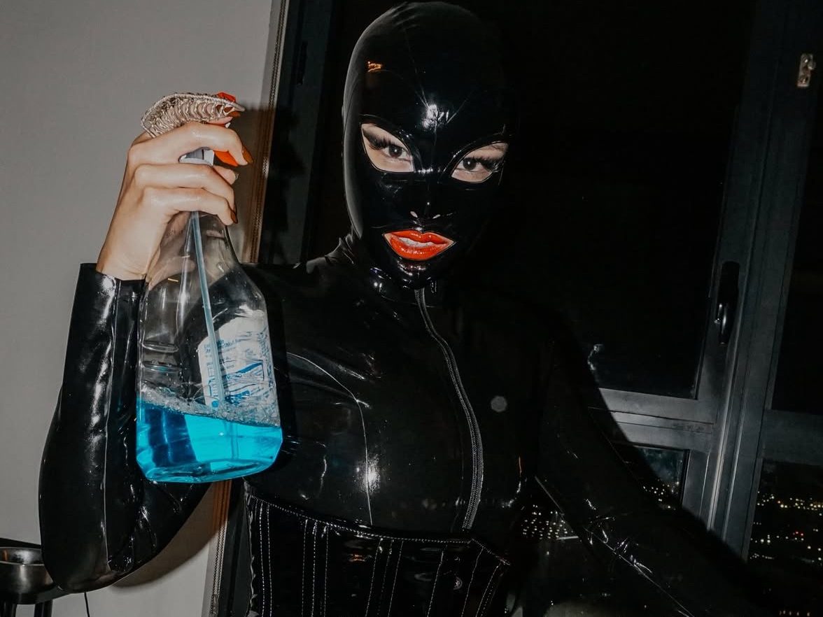 a domme wears a mask and holds a spray gun