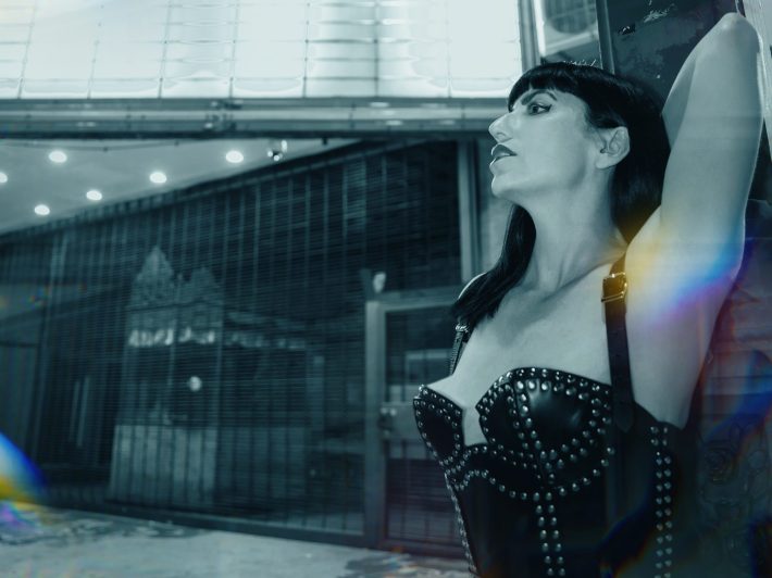 a woman in a studded corset poses in front of a theater