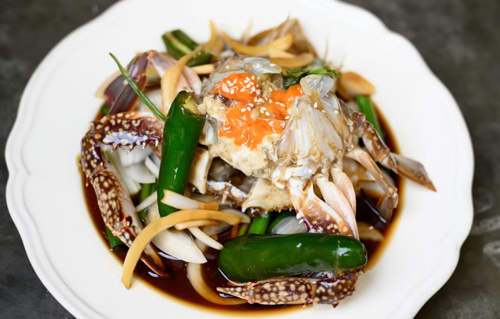 Soban’s ganjang gejang, marinated crab on a white plate topped with sesame seeds, chiles, and pickled carrot strips