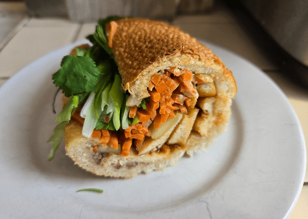 Half of a tofu banh mi sandwich with carrots, cilantro, and cucumber on a white plate