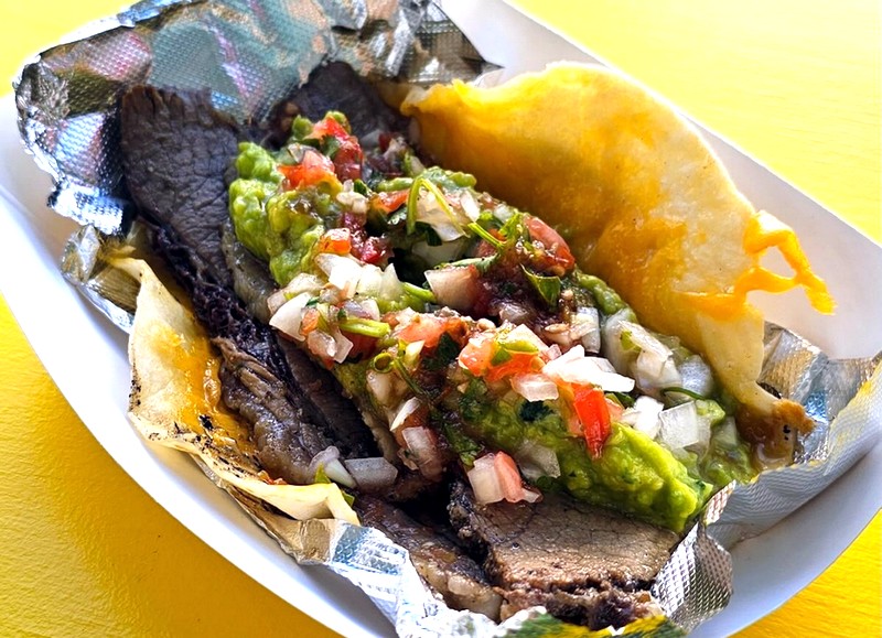 A brisket at Tacali Taco. topped with salsa mexicana and guacamole in a piece of tinfoil, which sits in a paper tray
