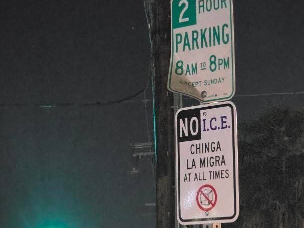 a sign made to look like a street sign posted: "NO ICE CHINGA LA MIGRA AT ALL TIMES"