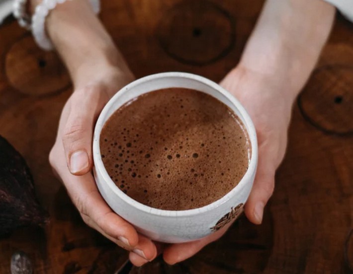 A white ceramic cup of hot chocolate being gripped on the side by two hands