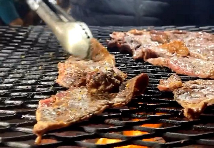 Asada grilling on an black iron grate over ofire at Tacos El Brother.