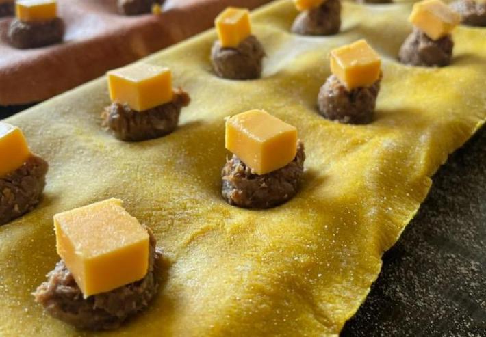A sheet of pasta with small raw beef balls topped with cubes of cheese