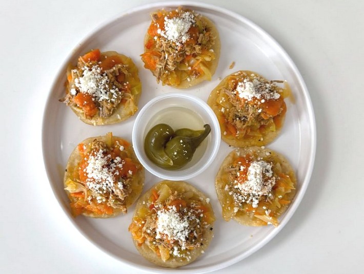 A white plate ringed with 5 Guatemalan garnachas topped with cheese, with a small container of chiles in the middle