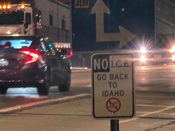 parking signs on a street along with one unofficial sign reading "NO I.C.E GO BACK TO IDAHO"