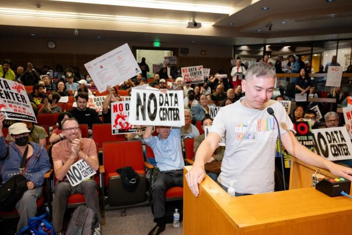 a man stands at a podium in front of a crowd of protestors