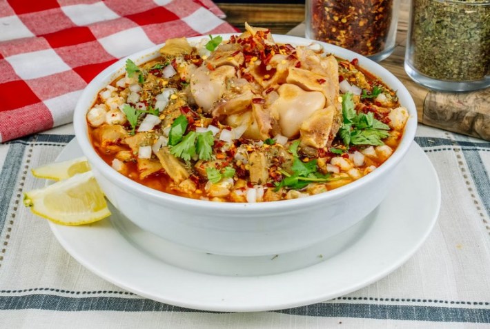 A big bowl of red menudo con pata at Mr. Menudo Oficial, with two lemon wedges on the side