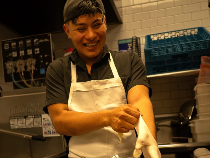 a man wearing an apron smiles while putting on dish gloves