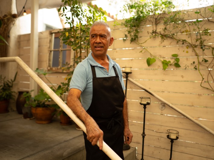 a man in an apron and blue polo stands on a staircase