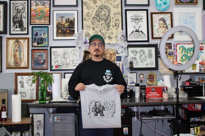 a man in glasses holds a t-shirt that shows a figure spray painting "FUCK ICE"