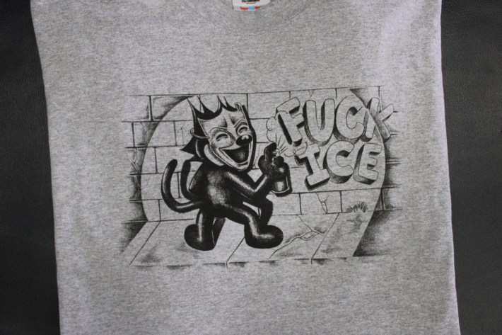 artwork of a figurine spray painting "FUCK ICE" onto a brick wall