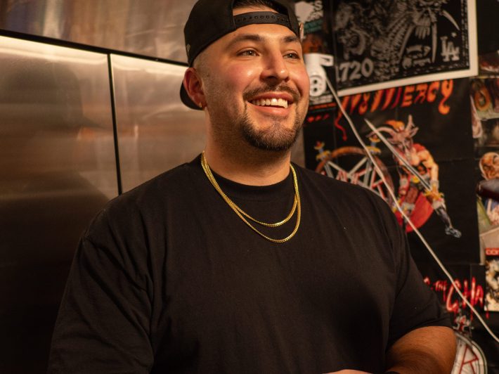 a man in a cap, shirt, and necklaces smiles