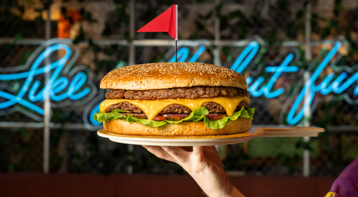 A massive 5-pound burger with a red flag at the top being held up by a hand