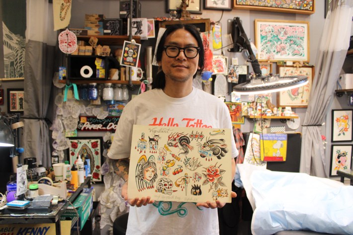 a man in glasses holds a tattoo flash sheet he has created
