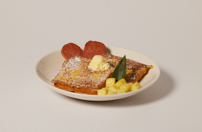 A white plate with butter-topped French toast, SPAM, and fruit.