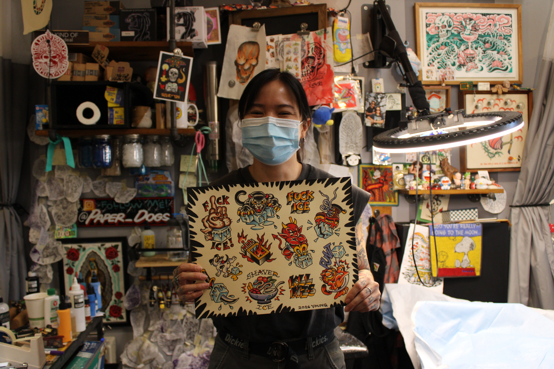 a woman with tattoos holds up a tattoo flash sheet she has created