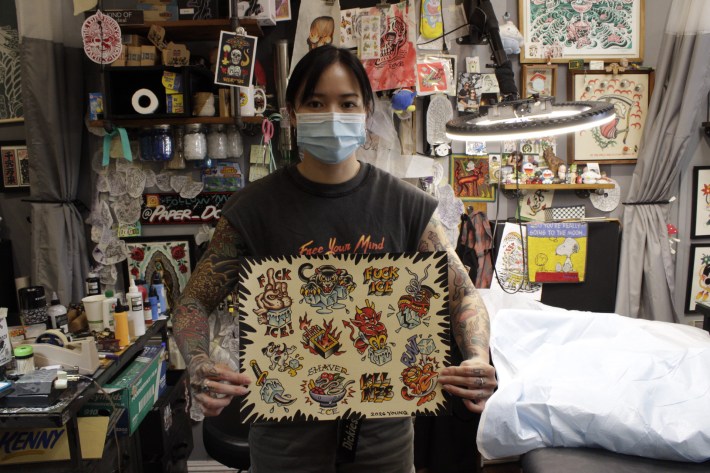 a woman with tattoos holds up a tattoo flash sheet she has created