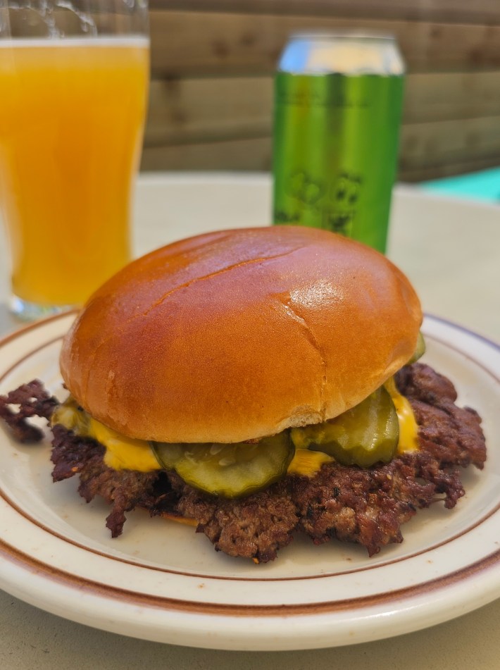 A burger on a plate next to a hazy beer.