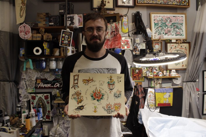 an artist holds a flash sheet they created in a tattoo shop