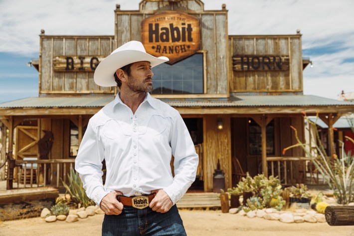 Actor Ian Bohen in front of an old west-style building that's sign says The Habit Ranch.