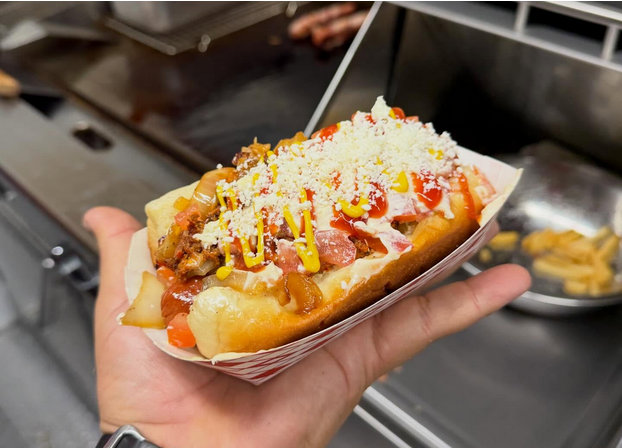 A cheese-sprinkled hot dog in a carton in someone's hand