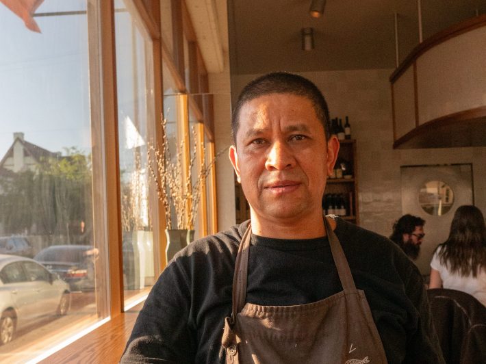 a man in an apron poses next to a window